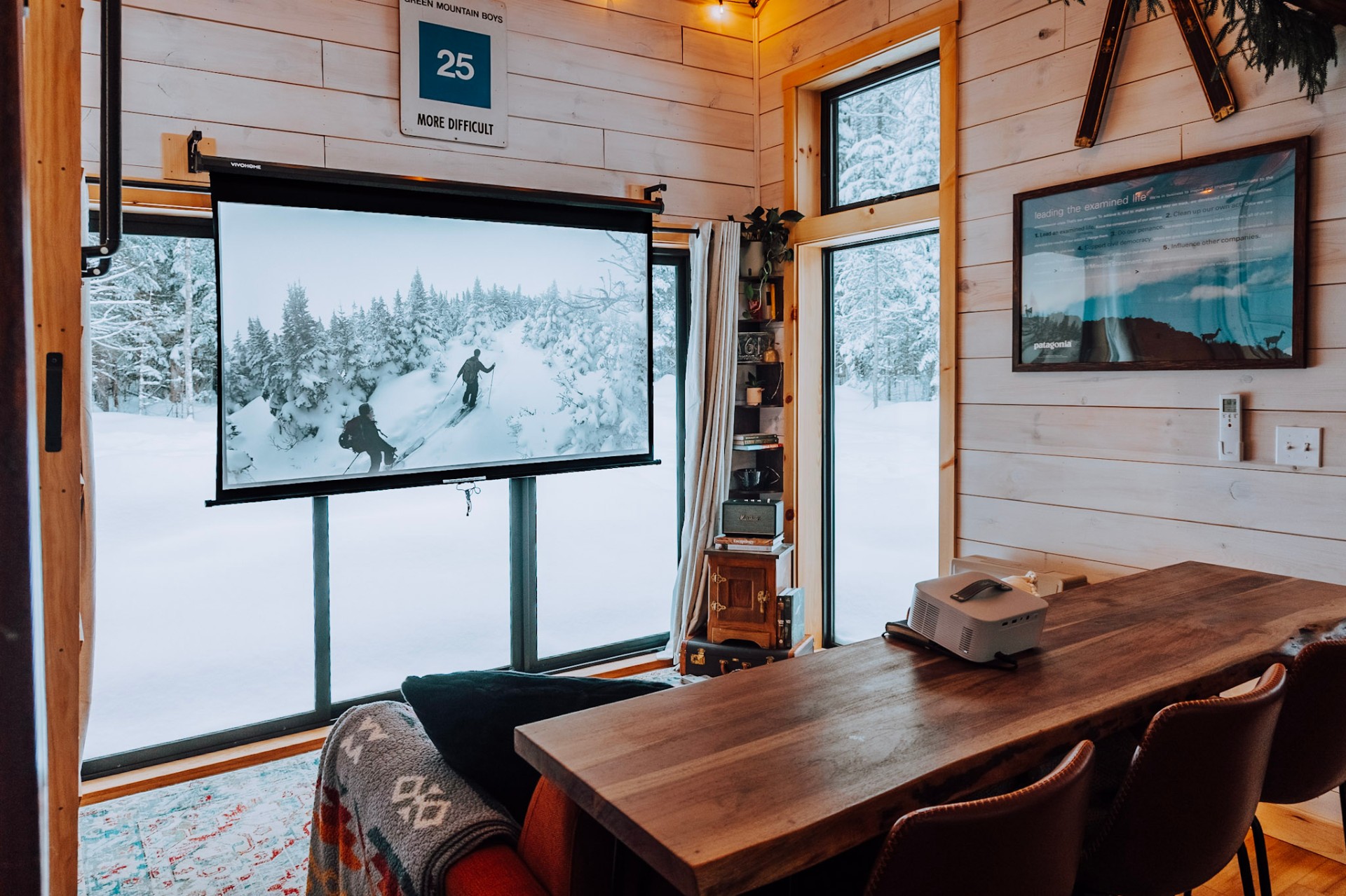 Cozy Vermont cabin interior with projector screen showing skiers and snowy forest views through large windows
