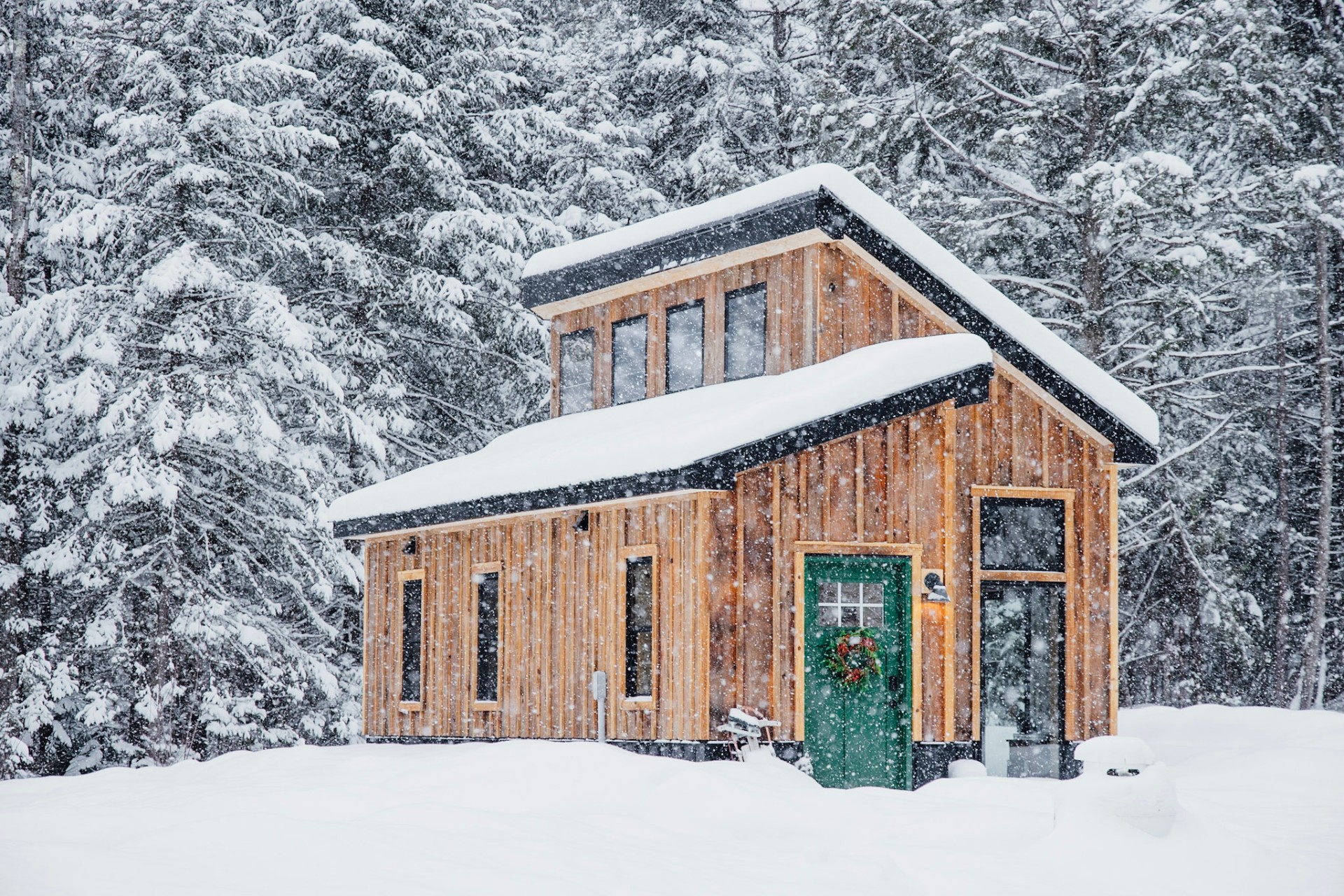 Modern wooden cabin with green door in a snowy Vermont forest during snowfall
