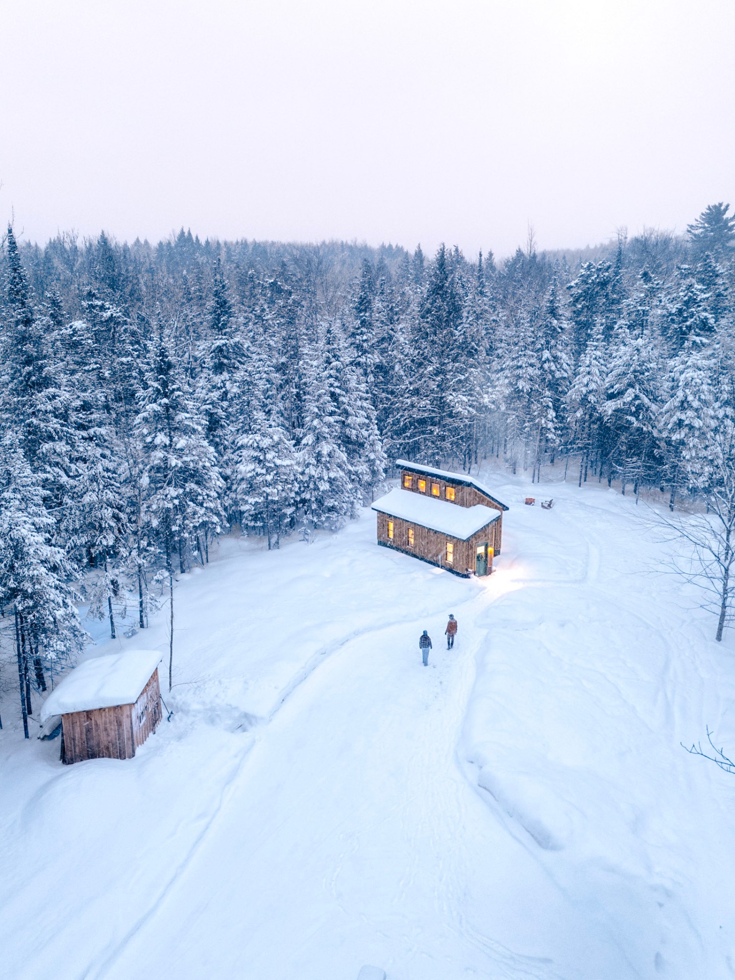 Aerial view of a wooden cabin in a snowy Vermont forest at dusk